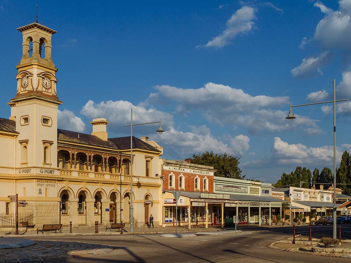 Historic post office building with clock tower in Beechworth, surrounded by shops and clear blue sky.
