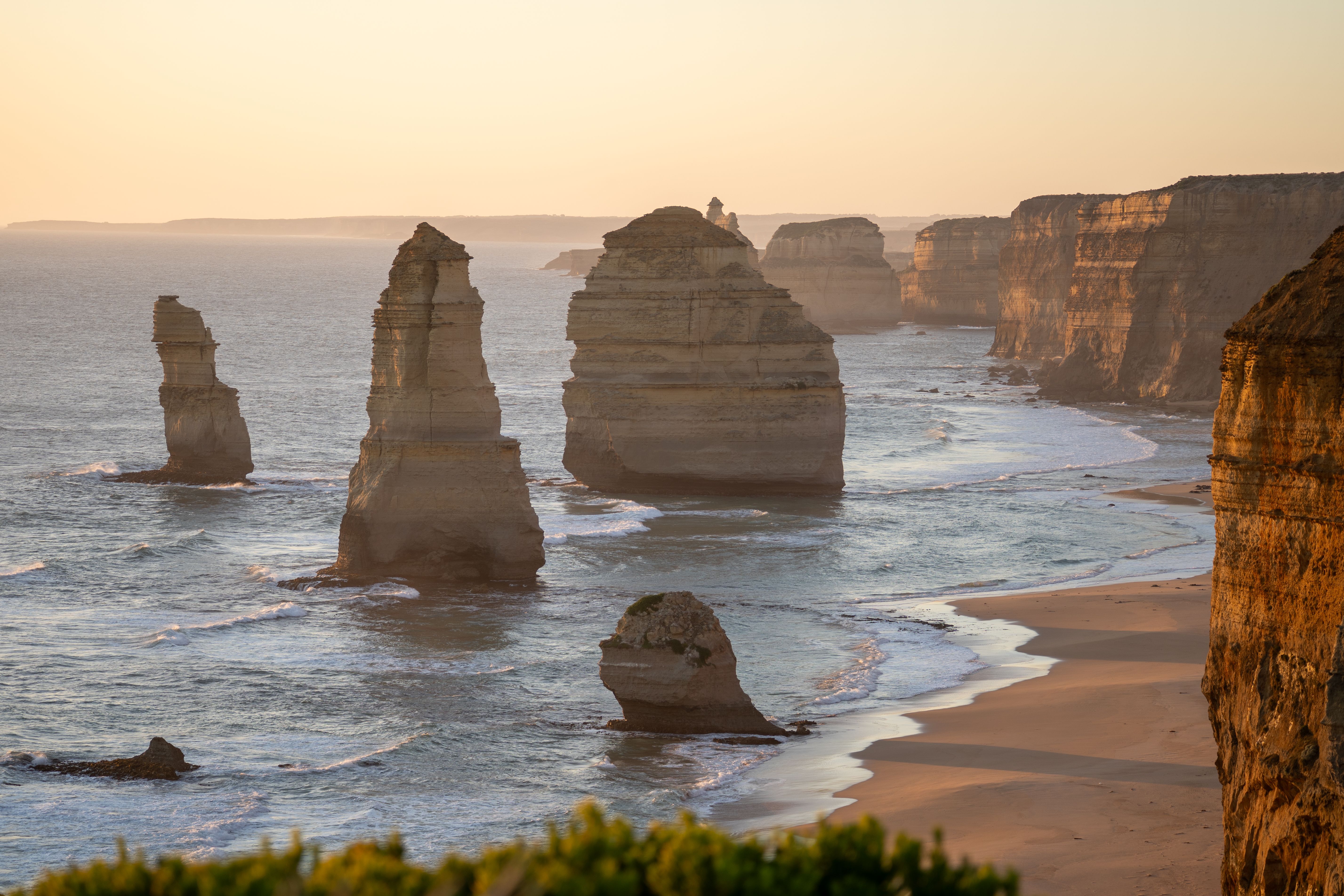 Scenic view of the Twelve Apostles rock formations along the rocky coastline, with waves crashing against the cliffs during sunset.